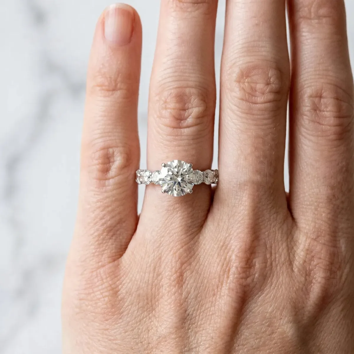 Round Cut Diamond Prong Setting with Side Stones on a Pave Band White gold